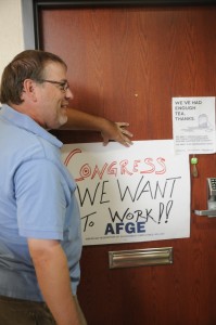 Jason Alexander, 17-year tax processor for the USDA, holds a sign against Rep. Ann Wagner's office door to be taped.